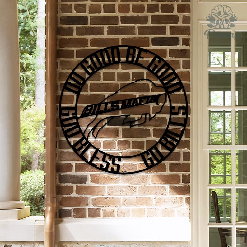 May include: Black metal wall art with the words "DO GOOD BE GOOD" and "LET GOD BLESS GO BILLS" in a circular design. The words "BILLS MAFIA" are in the center, with a hand holding a football. The art is mounted on a brick wall.