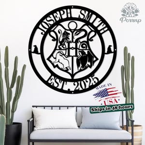 May include: Black metal family name sign with the name "JOSEPH SMITH" in a circular design. The sign includes a crest with animal figures and the text "EST. 2025". The sign is displayed on a white wall with a bench and plants.