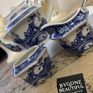 May include: A vintage tea set with a blue and white landscape design. The set includes a teapot, creamer, and sugar bowl. The pieces are made of porcelain and feature a detailed transferware pattern. The set is displayed on a wooden surface.
