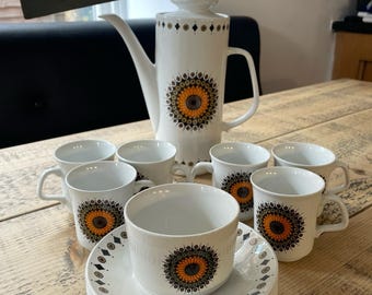 以下が含まれることがあります： オレンジ、黄色、黒の花柄が特徴の白いヴィンテージコーヒーセット。セットにはコーヒーポット、カップ、ソーサーが含まれています。「BYGONE & BEAUTIFUL VINTAGE & ANTIQUE」の文字が見えます。