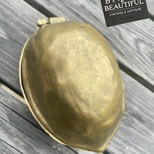 May include: A vintage brass container with a hinged lid. The container has a rounded, organic shape and a warm, golden hue. The text "BYGONE & BEAUTIFUL VINTAGE & ANTIQUE" is on a black tag.