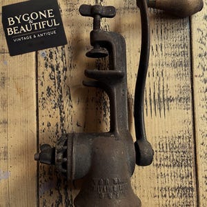 May include: Antique cast iron meat grinder with a wooden handle. The grinder has a crank and a metal plate with the text "Lyon Mfg. Co. Troy, N.Y."