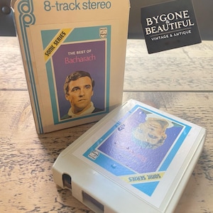 May include: A vintage 8-track stereo tape of "The Best of Bacharach." The white cassette has a blue and yellow label with a portrait of a man. The cassette case is white with the text "8-track stereo" and "Sonic Series."