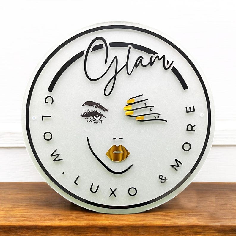 Może przedstawiać: Okrągły biały znak z czarnym napisem "Glam Glow, Luxo & More" ze stylizowaną ilustracją oka i ust kobiety z złotym lakierem do paznokci i ustami.