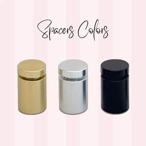 May include: Three cylindrical spacers in gold, silver, and black. Each spacer has a flat, circular top and a matching base. The text "Spacers Colors" is written in cursive script above the spacers.