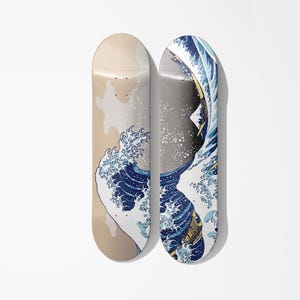 Op de afbeelding: Twee skateboards met een beige en blauw golfpatroon, geïnspireerd op Japanse kunst. De boards staan naast elkaar, met het golfpatroon in blauw en wit tegen een beige achtergrond.