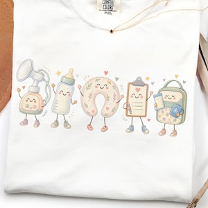 May include: A white t-shirt featuring a graphic print of five anthropomorphic baby-related items: a breast pump, a baby bottle, a nursing pillow, a clipboard, and a diaper bag, all with smiling faces, arms, and legs, accented by small hearts and stars.