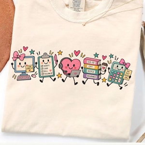 Op de afbeelding: Een crèmekleurig t-shirt met een afbeelding van cartoonfiguren voor medische facturering, waaronder een computer, klembord, hart met headset, een stapel boeken met de labels ICD-10, CPT, HCPCS, Insurance en een rekenmachine met roze strikjes.