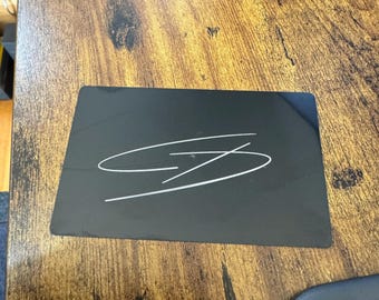 May include: A black rectangular mousepad with a white signature on it.