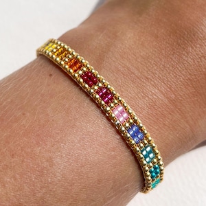 May include: A rainbow beaded bracelet. The bracelet is made up of small, colourful beads in a spectrum of colours, including yellow, orange, red, pink, blue, and green, set against a gold-coloured band. The bracelet is approximately 1.3 cm wide.