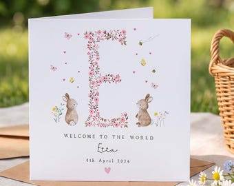 Può includere: Biglietto di auguri quadrato con un design floreale della lettera 'E', farfalle, api e due coniglietti. Il testo recita 'Benvenuto al mondo' con un nome e una data. Il biglietto è su una superficie bianca con una busta marrone.