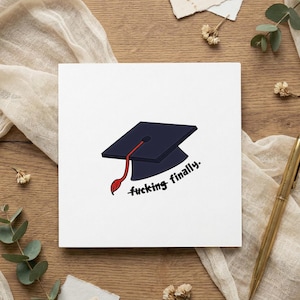Könnte beinhalten: Eine weiße Abschlusskarte mit einem marineblauen Doktorhut und einer roten Quaste. Der Text "fucking finally" ist in schwarzer Schrift geschrieben. Die Karte liegt auf einer Holzoberfläche mit einem goldenen Stift und Dekorationselementen.