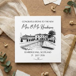 Op de afbeelding: Vierkante trouwkaart met een zwart-wit illustratie van een statig huis en een waterpartij. De tekst luidt "Gefeliciteerd aan de nieuwe Mrs & Mr Henderson" en "Elmridge Hall, Schotland 21 juli 2026". Een gouden pen is zichtbaar.