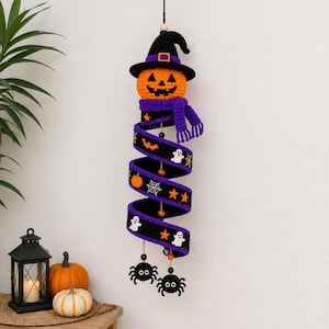 May include: A hanging crochet Halloween decoration featuring an orange jack-o'-lantern head wearing a black witch hat and a purple scarf. Below, a black spiral ribbon displays white ghost, orange pumpkin, spiderweb, and star motifs, ending with two black spider ornaments.