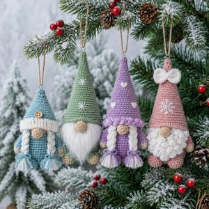 Könnte beinhalten: Vier gehäkelte Wichtel-Ornamente hängen an einem Tannenbaum. Der erste ist blau mit weißen Zöpfen, der zweite grün mit weißem Bart, der dritte lila mit weißen Zöpfen und Herzen, und der vierte ist rosa mit einem weißen Bart und einer Schleife.