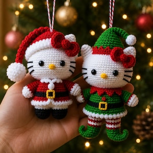 May include: Two crocheted ornaments featuring a white cat character. One wears a red Santa hat and suit with a black belt and gold buckle. The other wears a green elf hat and outfit with a red collar, black belt, gold buckle, and striped leggings.