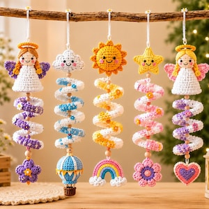 May include: Five hanging crochet ornaments suspended from a wooden branch. The set includes two angels, a cloud, a sun, and a star, each featuring a spiral tail ending in a unique shape like a flower, hot air balloon, rainbow, or heart.