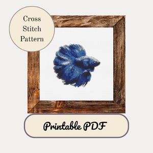 Puede incluir: Un patrón de punto de cruz de un pez betta azul, enmarcado en un marco de madera rústica. El texto "Cross Stitch Pattern" está en un círculo en la esquina superior izquierda. El texto "Printable PDF" está en un rectángulo redondeado en la parte inferior.