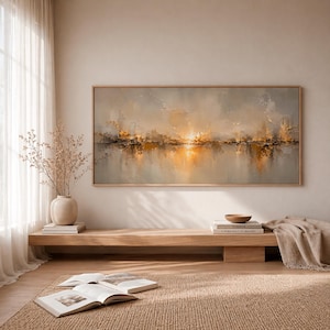 May include: A rectangular landscape painting in a light wood frame featuring an abstract sunset scene with warm golden, orange, and soft gray tones. The artwork depicts a glowing horizon line with textured brushstrokes reflecting light.