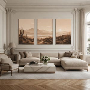 Può includere: Tre stampe artistiche verticali incorniciate che raffigurano un paesaggio desertico con montagne, cactus e un sole al tramonto in tonalità beige e marrone. Le opere sono esposte in fila sopra un grande divano angolare beige e un tavolino in marmo.