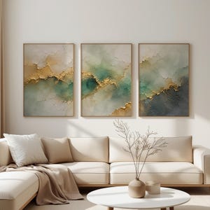 Könnte beinhalten: Ein Set aus drei rechteckigen Wandbildern mit einem abstrakten Design in gemischten Farbtönen von Salbeigrün, Creme und Weiß, akzentuiert durch strukturierte Goldfoliendetails. Jedes Bild ist in einem dünnen, hellen Holzrahmen eingefasst.