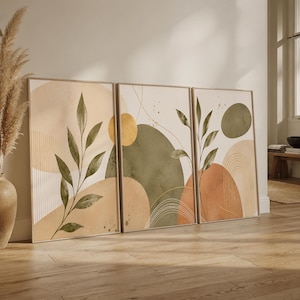 Könnte beinhalten: Ein Set aus drei gerahmten Wandbildern mit abstrakten Formen in Salbeigrün, Terrakotta und Beige. Die Motive zeigen botanische Blattillustrationen, feine Linienbögen und kreisförmige Elemente auf einem hellen, cremefarbenen Hintergrund.