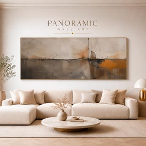 Könnte beinhalten: Panoramische Wandkunst mit einer neutralen Farbpalette. Das abstrakte Gemälde zeigt ein strukturiertes Design in Beige-, Braun- und Orangetönen, gerahmt in Gold. Das Kunstwerk hängt über einem beigefarbenen Ecksofa in einem modernen Wohnzimmer.