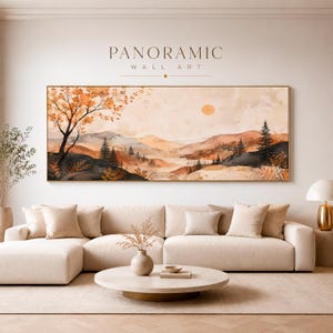 Könnte beinhalten: Ein panoramisches Wandkunstbild mit einer Landschaft aus hügeligen Bergen, Kiefern und einem großen Baum mit orangefarbenen Herbstblättern. Die Szene zeigt eine blasse Sonne an einem weichen Himmel in den Farben Orange, Beige und Dunkelbraun.
