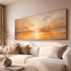 Könnte beinhalten: Ein großes rechteckiges Landschaftsgemälde in einem dünnen goldenen Rahmen zeigt einen abstrakten Sonnenuntergang mit leuchtend orangefarbenen, gelben und weichen grauen Wolken, die sich über einer ruhigen Horizontlinie spiegeln, an einer Wand.