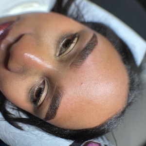 Puede incluir: Primer plano del rostro de una persona, centrado en las cejas. Las cejas son oscuras y bien definidas, con una curvatura natural. La piel es suave y tiene un ligero brillo. Los ojos están abiertos y las pestañas son visibles.