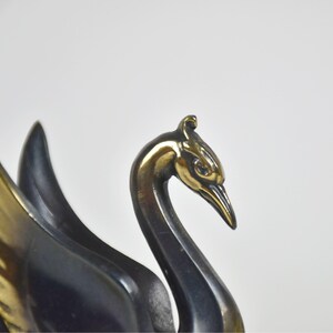 May include: A close-up of a bronze swan sculpture. The swan's head and beak are a shiny gold color, while the neck and body are a darker bronze. The wings are partially visible, with gold and dark bronze feathers.