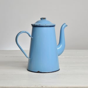 Peut inclure: Une cafetière en émail bleu clair avec une poignée et un bec verseur incurvés. Le pot de style vintage a un couvercle et une bordure bleu foncé. Un article de cuisine classique.