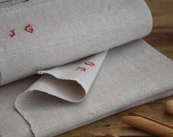 May include: Two pieces of off-white linen fabric with red embroidered numbers, "1" and "6", on the top piece.
