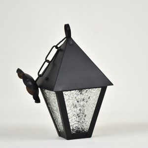May include: Black metal hanging lantern with a clear, textured glass panel. The lantern has a decorative metal finial and a chain for hanging.