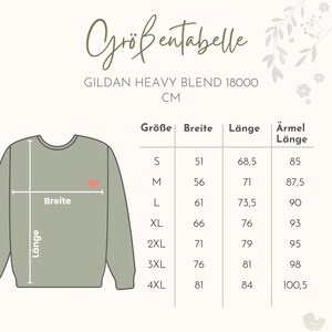 Puede incluir: Una sudadera verde salvia Gildan Heavy Blend 18000 con un gr&aacute;fico de coraz&oacute;n. La imagen incluye una tabla de tallas en cent&iacute;metros, que muestra las medidas para las tallas S a 4XL. La tabla detalla el ancho, el largo y el largo de la manga.