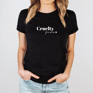 Op de afbeelding: Zwart T-shirt met de witte tekst "Cruelty Free". De top met korte mouwen heeft een ronde hals. De woorden zijn in een cursief lettertype geschreven en gecentreerd.