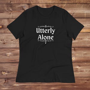 Könnte beinhalten: Schwarzes T-Shirt mit einem weißen Aufdruck, der in einer dekorativen Schrift "Utterly Alone" sagt.