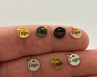 May include: Six round metal charms with a jump ring. Each charm is a different color: gold, black, silver, rose gold, brass, and gunmetal. The charms have the word "Logo" engraved on them.