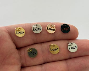 Puede incluir: Siete abalorios redondos de metal con un anillo de salto. Cada abalorio es de un color diferente: oro, plata, oro rosa, negro y tres tonos de bronce. Los abalorios tienen la palabra "Logo" impresa en negro.