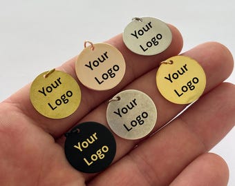 Puede incluir: Seis dijes metálicos circulares en varios acabados, incluyendo oro, oro rosa, plata, plata mate y negro. Cada dije cuenta con una pequeña argolla en la parte superior y el texto negro Your Logo grabado en el centro de la superficie.