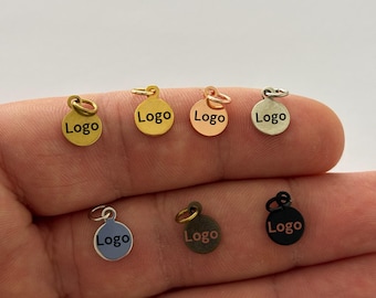 May include: Six round metal charms with a jump ring. Each charm is a different colour: gold, rose gold, silver, black, blue, and copper. The charms have the word "Logo" engraved on them.