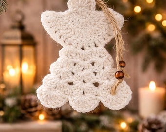 May include: A crocheted angel Christmas ornament in off-white hangs from a pine branch. The ornament has a detailed, textured design and is suspended by a natural twine. Two wooden beads dangle from the twine. The background features soft lighting and other holiday decorations.