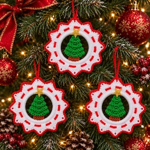 May include: Three circular crochet ornaments featuring a white scalloped border with red stitching. Each ornament contains a green crocheted Christmas tree with a brown trunk and a small gold glitter star at the top, suspended by a red yarn loop.