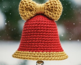 May include: A handmade crochet bell ornament with a red body and gold trim. A gold bow is attached to the top. A small silver bell hangs from the bottom. The background is a blurred winter scene.