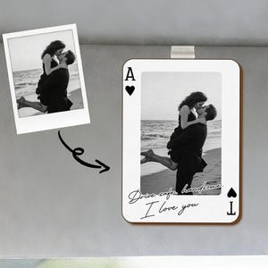 Könnte beinhalten: Ein Auto-Lufterfrischer in Form einer Spielkarte mit einem Schwarz-Weiß-Foto eines Paares am Strand. Die Karte zeigt das Pik-Ass-Symbol und den Text "Drive safe handsome, I love you."