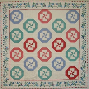 May include: A white quilt with a repeating pattern of red, blue, and green octagons with a white windmill design inside each octagon. The quilt is bordered with a blue, green, and white floral design.