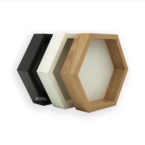 Peut inclure: Trois étagères hexagonales en noir, blanc et bois naturel. Les étagères sont empilées les unes sur les autres et sont conçues pour être montées au mur.