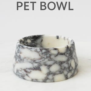 Puede incluir: Un cuenco para mascotas de m&aacute;rmol con un dise&ntilde;o &uacute;nico. El cuenco es blanco con vetas grises, y el texto "MARBLE PET BOWL" se muestra encima. El cuenco est&aacute; hecho de un material s&oacute;lido y tiene un acabado liso.