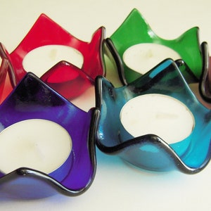 May include: A collection of six colorful glass candle holders. Each holder is a different color: red, purple, green, blue, and brown. Each holder contains a white tea light candle. The holders have a unique, petal-like shape.