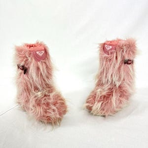 Puede incluir: Un par de botas de piel rosa con ribete de piel blanca. Las botas tienen un logotipo en el lateral que dice "ROXY".